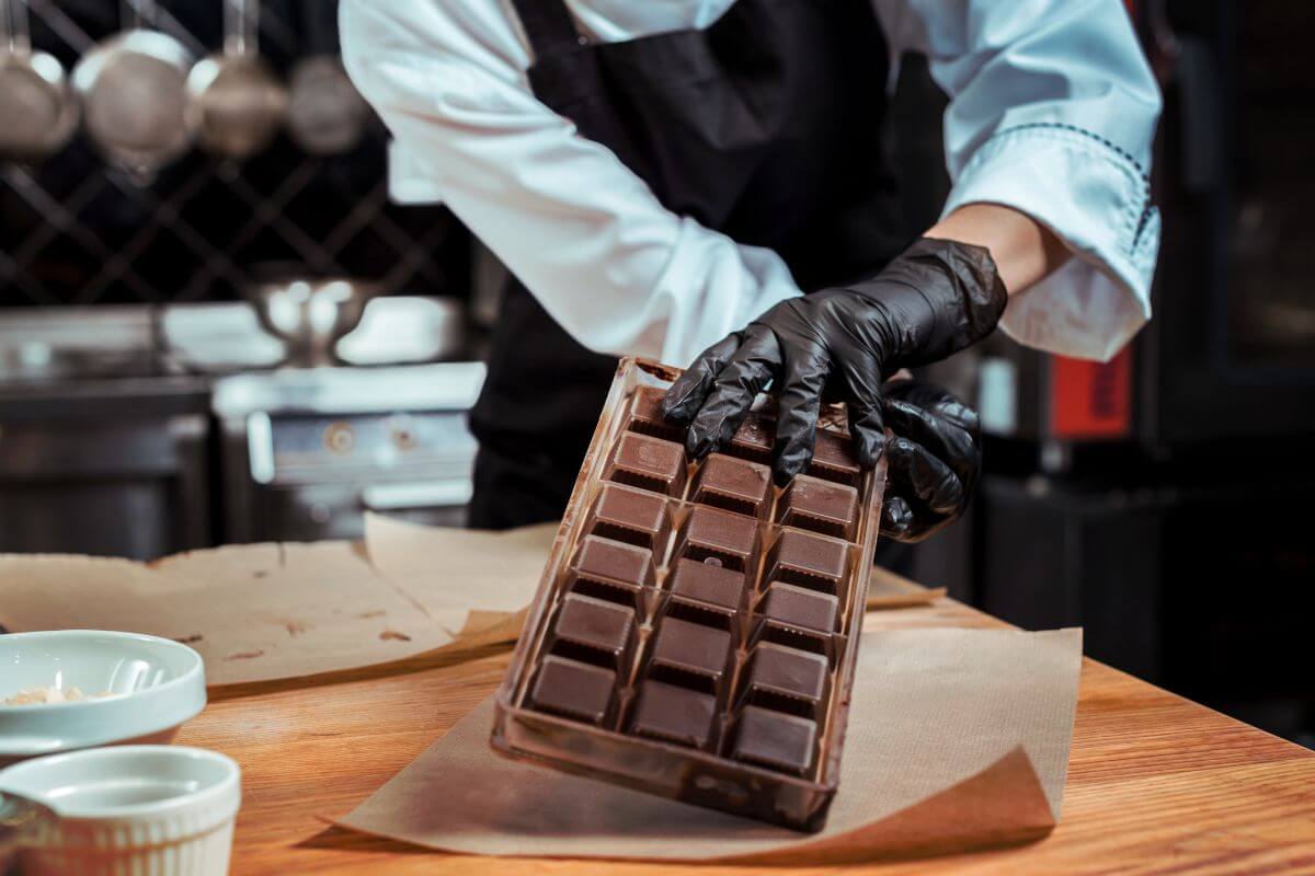 The photo tells about cups and a man wrapping the chocolate with paper indicating to swap store-bought chocolates for homemade treats which is a thoughtful way to show love without paying extra for fancy packaging.