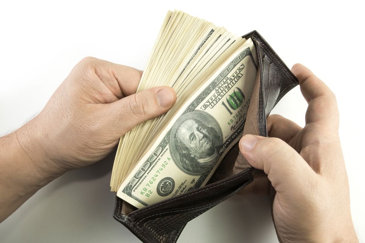Image of a man's hand with lots of money in his wallet.