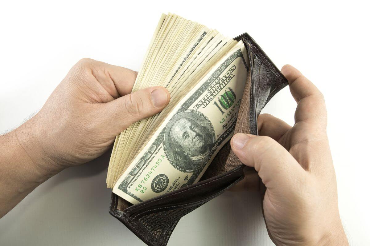 The photo shows a man's hand holding a wallet with a lot of dollar bills which means by 60 striving for 8-10x your salary gives you a strong chance of a stress-free retirement.