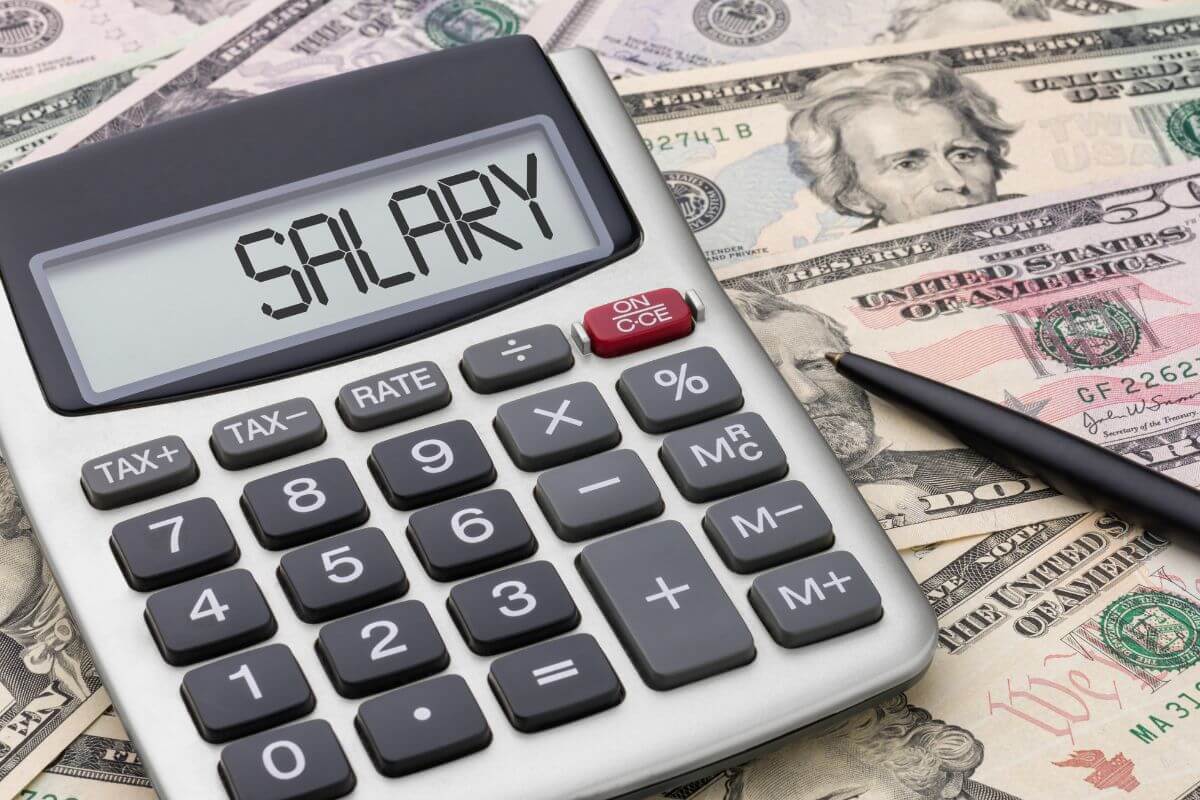 The picture shows a calculator with a note, a pen, and dollar bills scattered referring to 50 Having at least 6x your salary saved helps you keep on track.