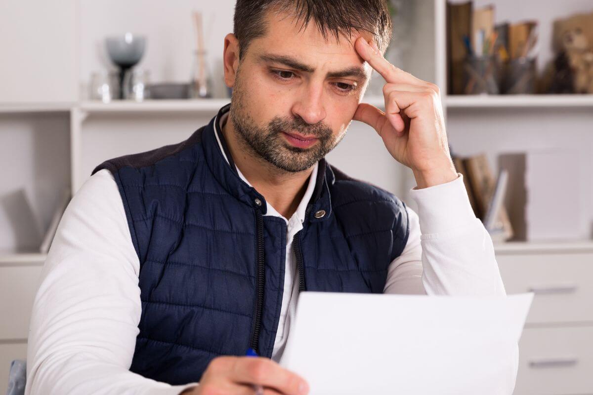 The image shows a man looking at the paper with a sad emotion which refers to asking for a hardship program to lower interest rates, reduce payments, or pause fees for a while.