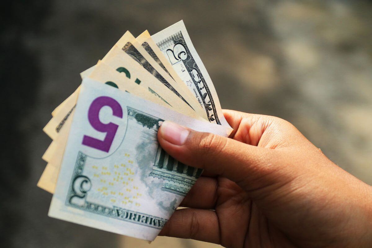 The photo of a girl's hand holding dollar bills indicating to start round up payments and putting the difference toward debt can help shrink debt faster.