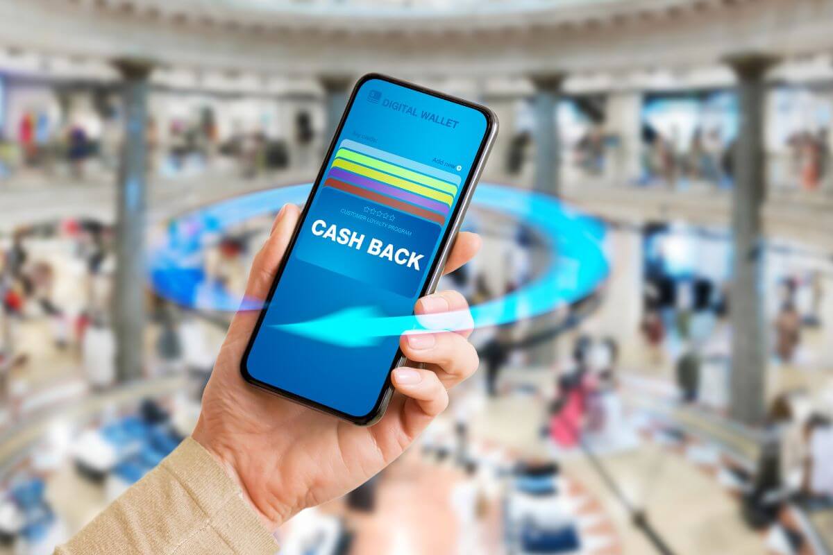 The image tells about a girl's hand holding a phone with a screen display referring to the use of cashback apps on every purchase which goes straight to debt.