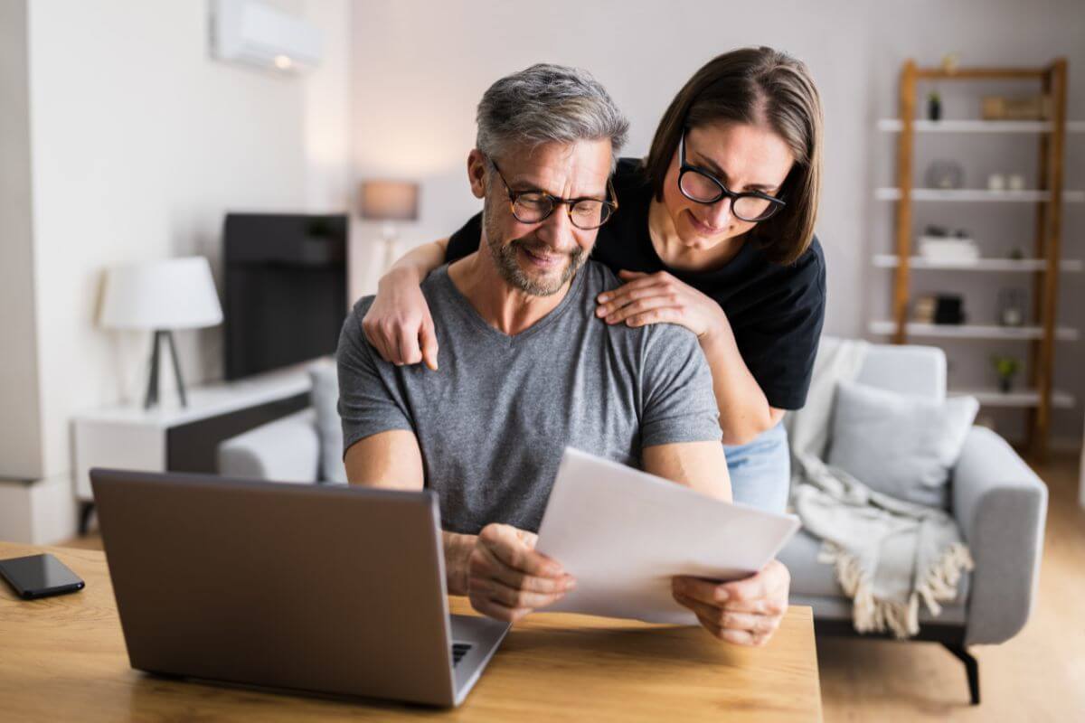 The picture shows a laptop on the tables and a couple looking at the papers which means finding an accountable buddy can help you keep on track and make it less stressful.