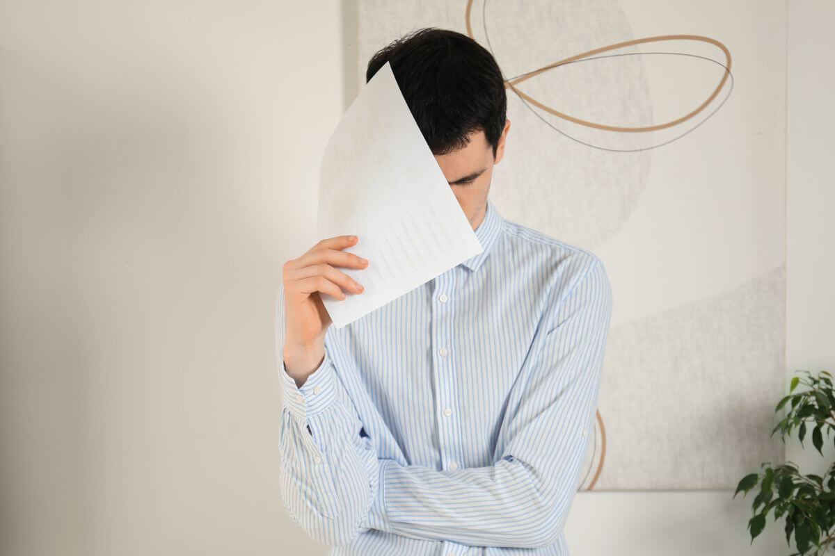 The photo shows a man covering his face with a piece of paper which means don't be embarrassed for being behind in savings, setting aside a few dollars can make a difference over time.