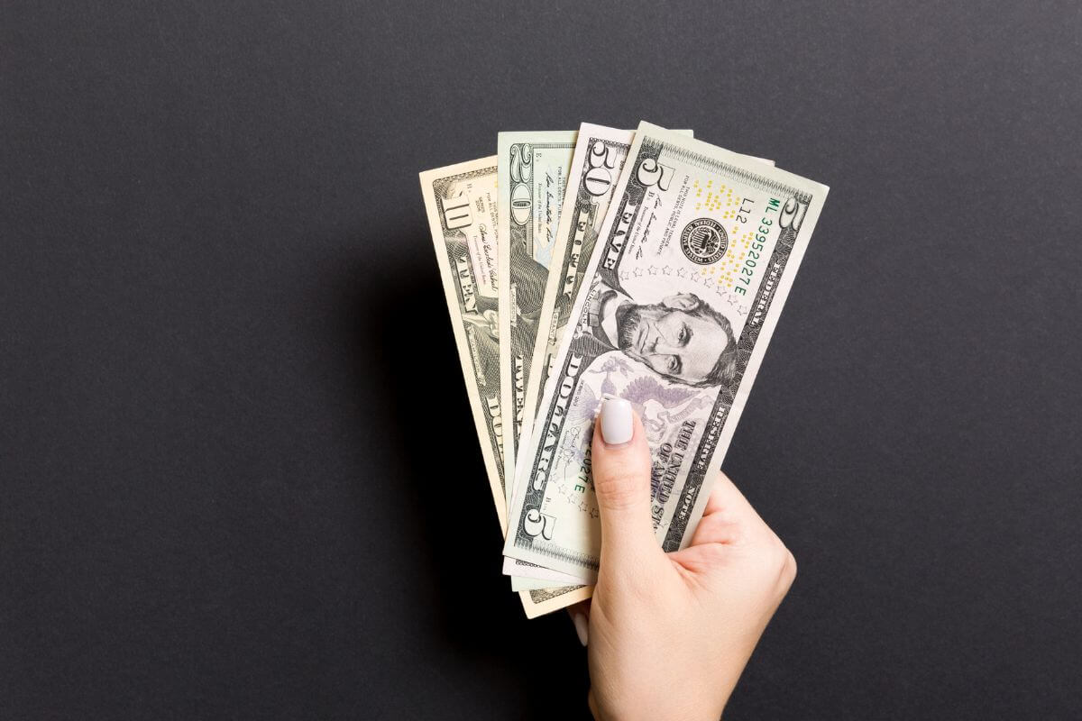 The photo shows a girl's hand holding dollar bills which means using the pay yourself first rule to create a habit of prioritizing your future.