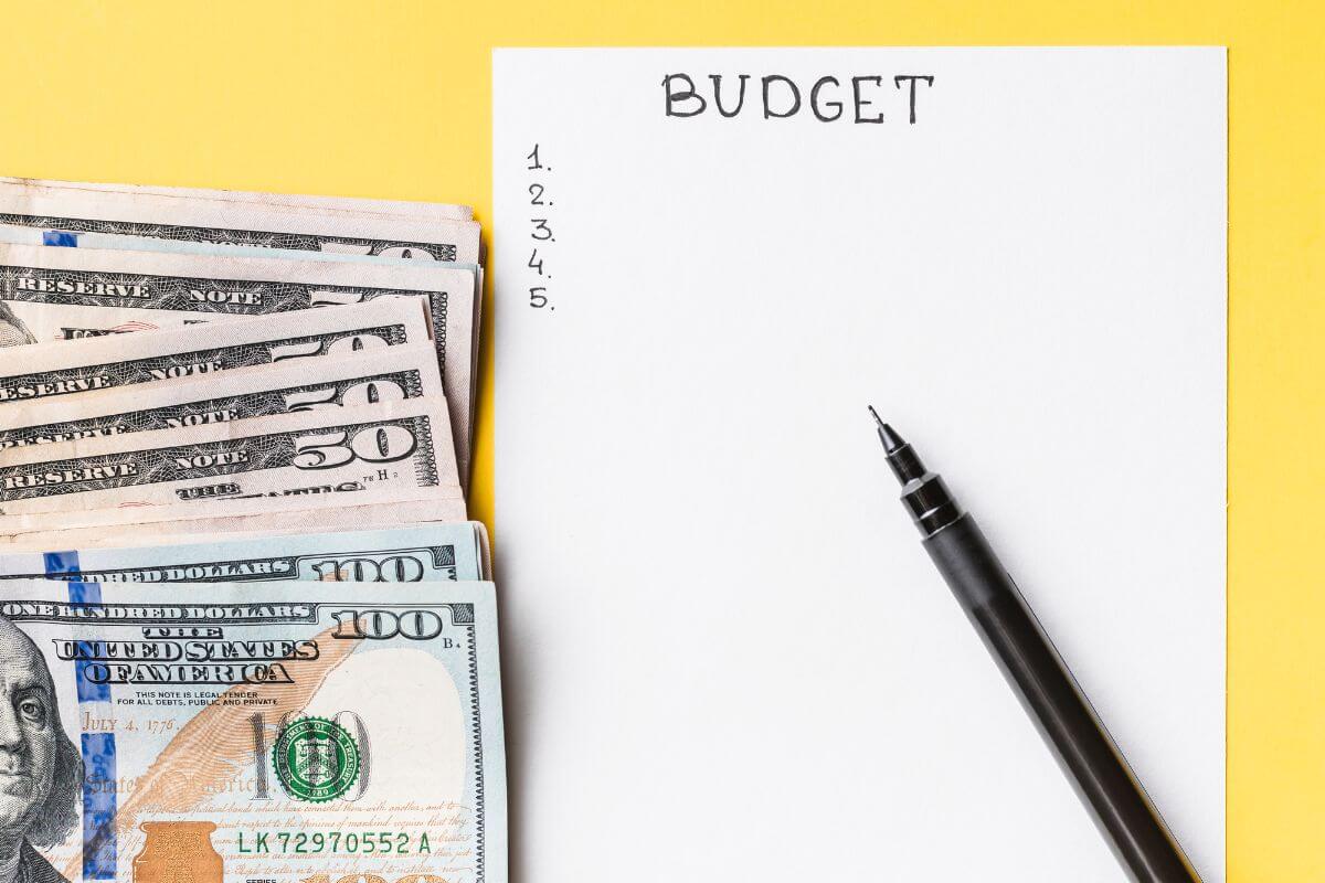 The picture shows a pen, dollar bills, and a piece of paper with notes indicating to find money in your budget so spare change goes straight to your account.