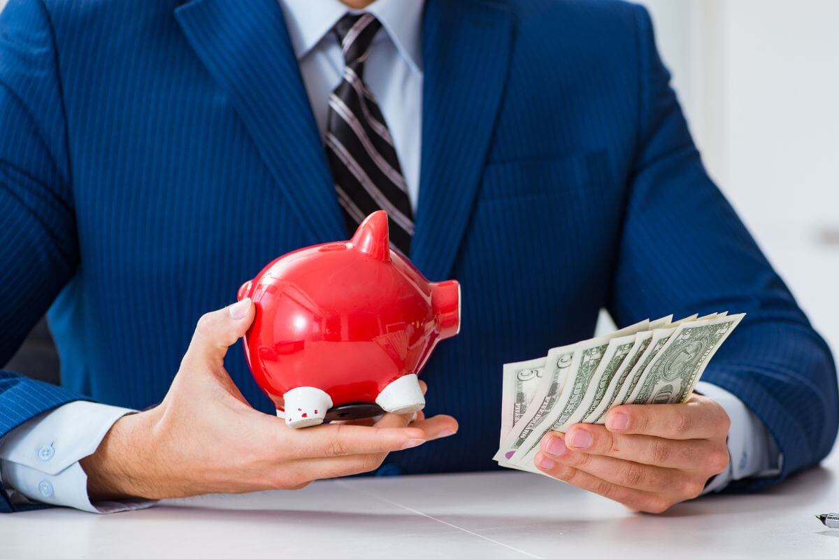 The picture tells about a man in a suit holding dollar bills and a piggy bank indicating to think of savings as buying freedom that can lead to big opportunities later.