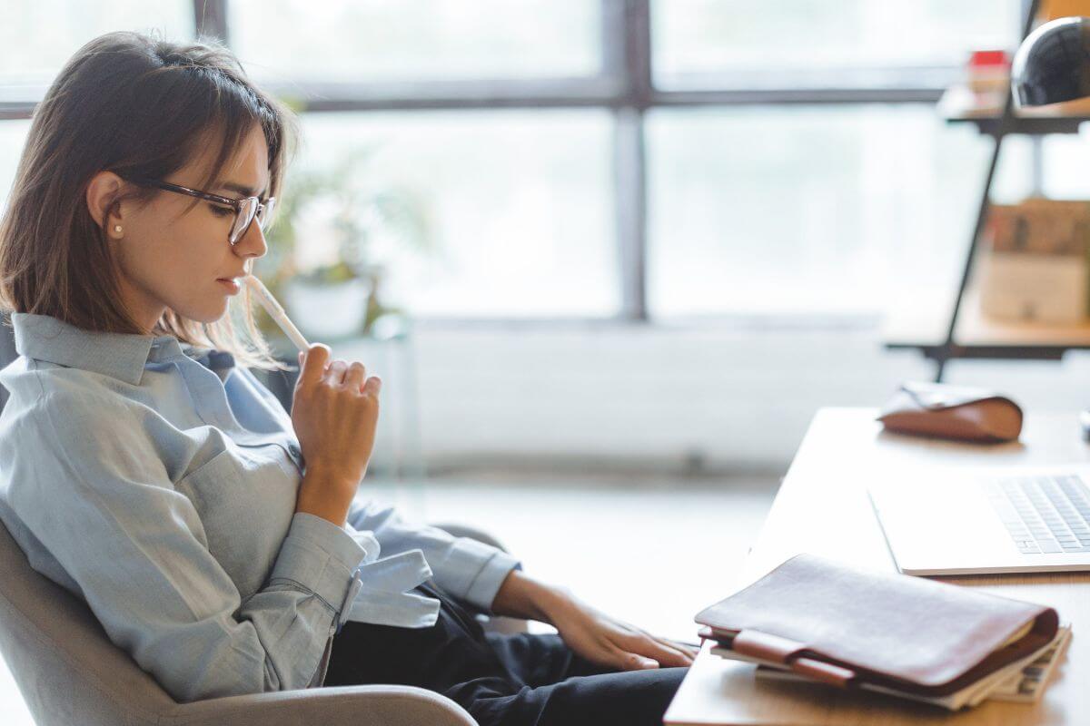 The image tells about a laptop, a notebook, and a girl thinking deeply referring to comparing yourself only to yesterday not others won't help you.