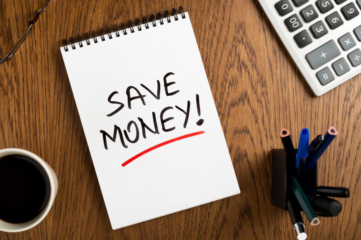 The picture shows a calculator, pens, a coffee, and a notebook with notes referring to starting this biweekly money savings challenge to grow your financial security step by step.
