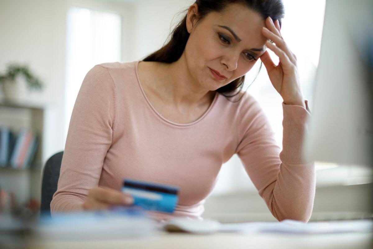 The photo shows a girl holding a credit card while looking at the papers referring to paying off all high-interest debts to free up money for other expenses and avoid draining your wallet.