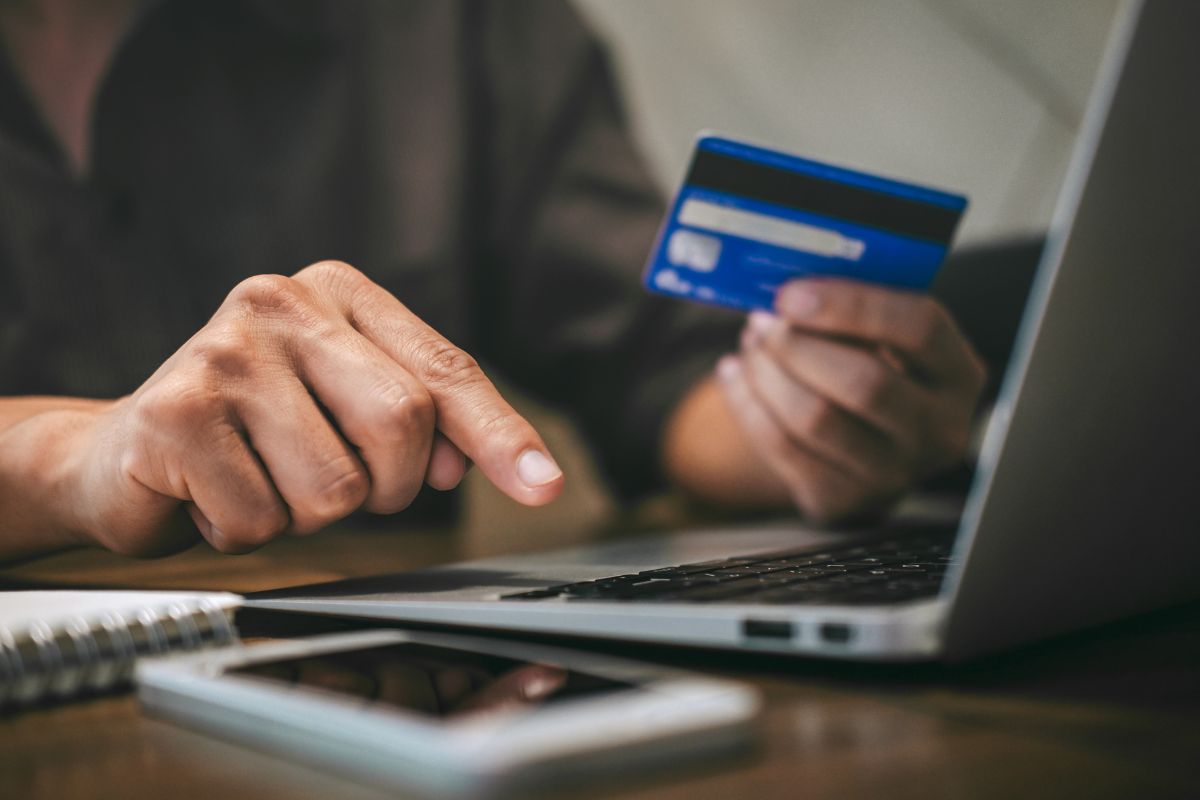 The image shows a phone, a notebook, and a man's hand typing on the laptop while holding a credit card, which means that opening a store credit card responsibly can help if you have bad credit.