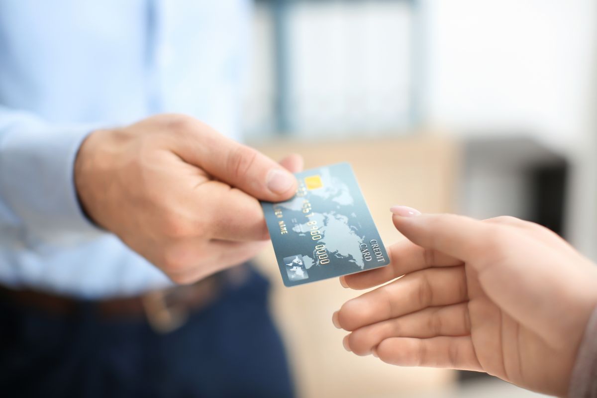 The image shows a man's hand handing a credit card to a girl's hand, which means becoming an authorized user on a responsible person's credit card could give your score a boost.