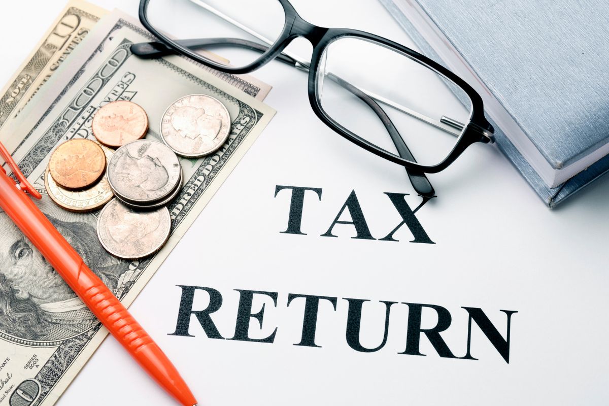 The photo tells about a notebook, coins, dollar bills, a pen, and a piece of paper with notes referring to filing a tax return even if not required to get money back and helps cover books, rent, and other expenses.