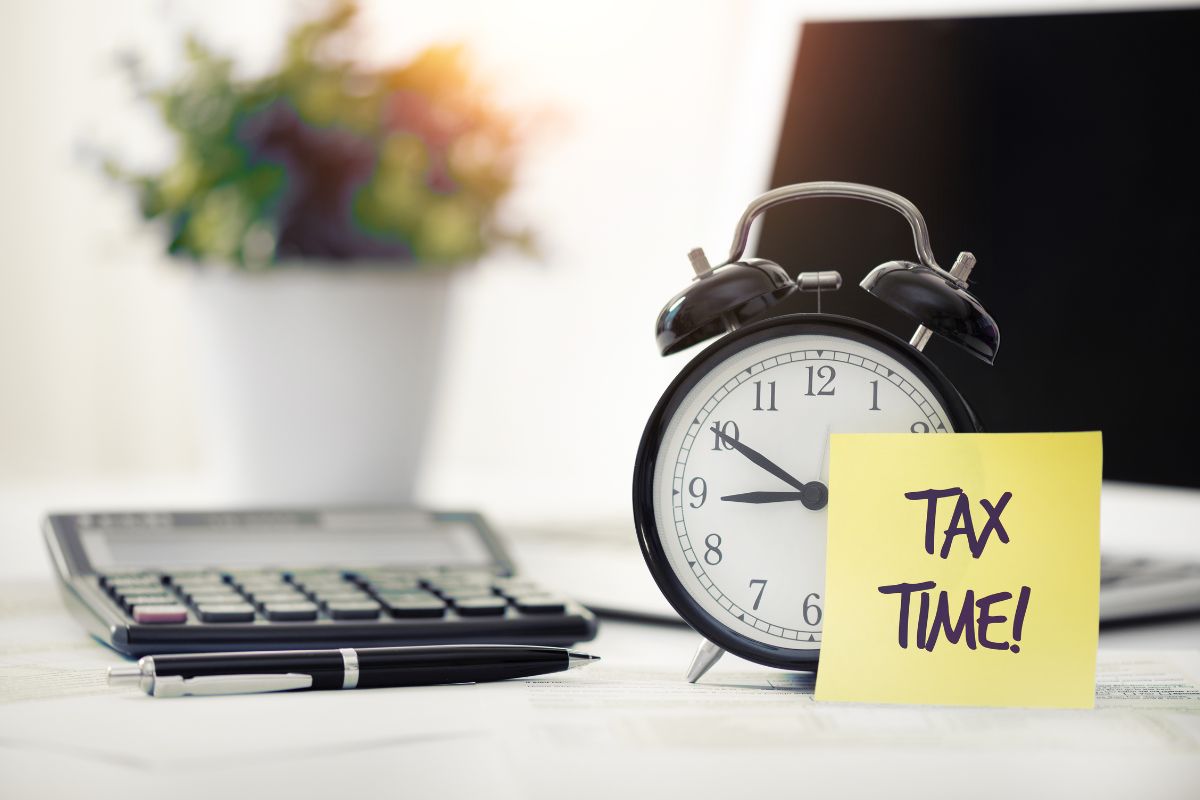 The photo tells about a calculator, a pen, a clock, and a piece of paper with notes indicating that avoiding missing tax deadlines helps you file on time, avoid stress, and ensure you get a refund sooner.