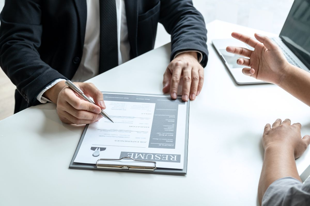 The image shows a laptop, a man in a suit pointing to the resume, and an applicant talking which means showcasing side projects makes your resume more complete and can help prove you're still learning and improving.