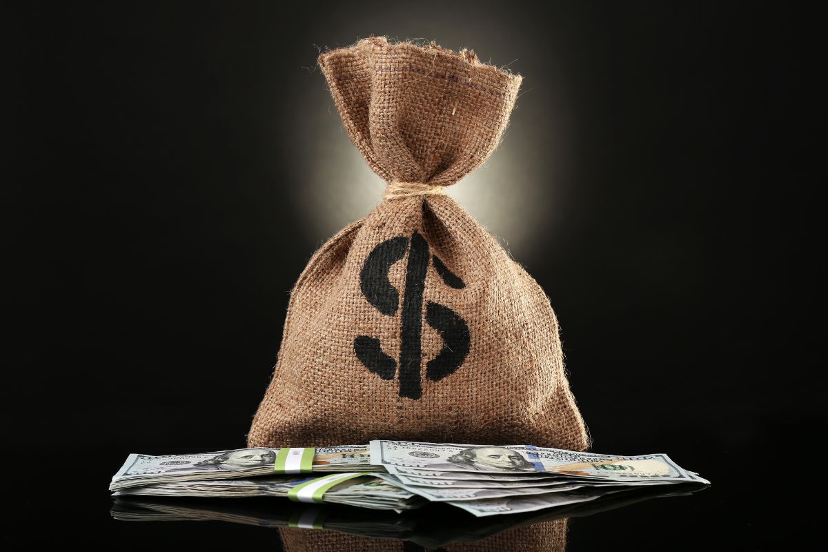 The image shows a bag with a dollar sign and dollar bills which means to make $200k a year your next with these guides that can you reach that income level faster.
