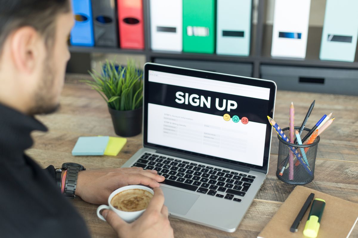 The image shows a plant, pens,  sticker notes, a notebook, markers, and a man having a coffee while using a laptop, referring to sign up for rent and utility reporting services to help build a stronger credit history.