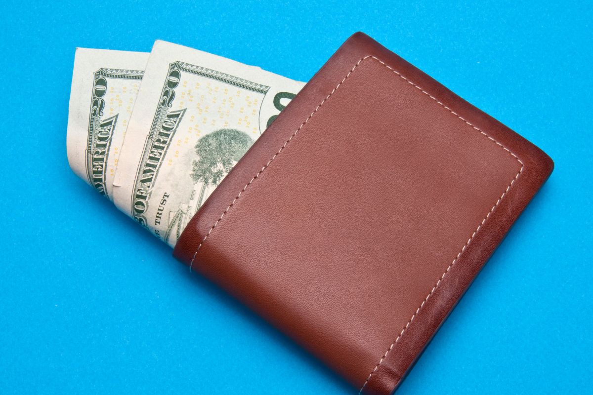 The photo shows a wallet with dollar bills indicating to use of a challenging budget by setting a no-spend month to reset finances and boost spending habits.