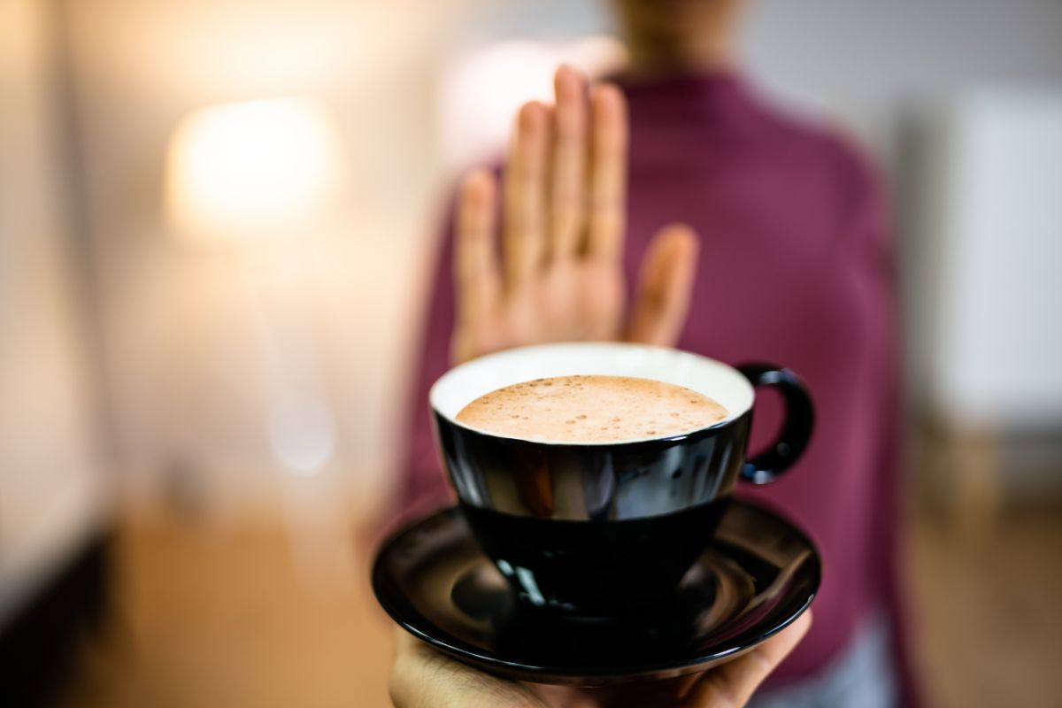 The photo shows a girl's hand holding a cup of coffee and a girl doing a stop sign which means creating a fun trade-off by cutting certain expenses and funding it to your goals to help your finances and enjoy goals.