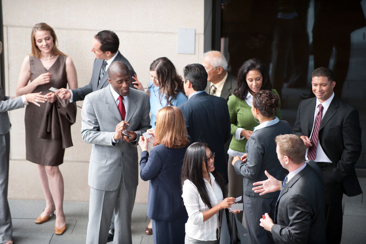The image shows a group of people having a conversation which means networking strategically with high-value people can lead to business deals, investments, and new income streams.