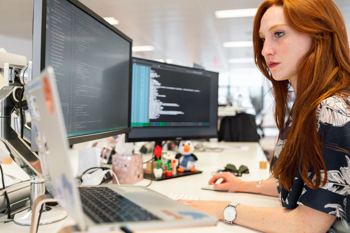 The photo shows a girl working on computers and a laptop referring to monetizing skills such as coding which brings in six figures or more and is one of the fastest ways to a rich life.