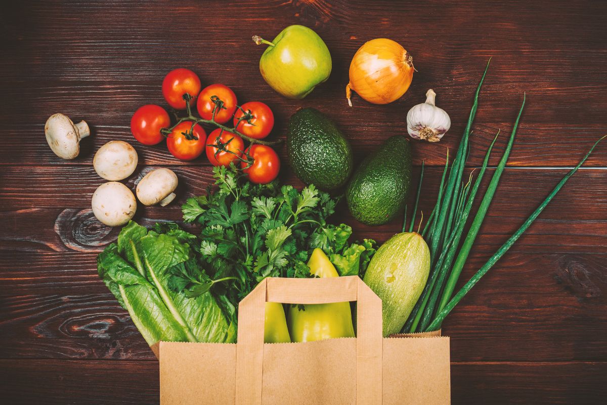 The photo shows a paper bag with different types of vegetables indicating that buying ugly produce is a great way to save money on groceries while cutting down on food waste.