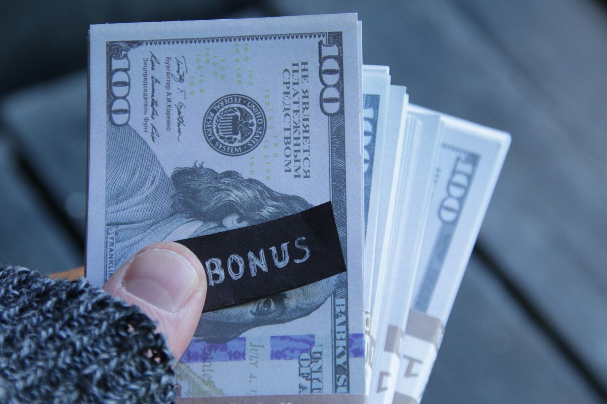 The photo shows a girl's hand holding dollar bills and a small piece of paper with a note referring to turning your job into an investment and buying wealth while you work.