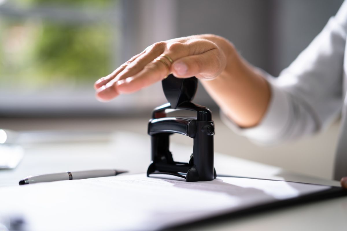 The image shows a pen and a girl's hand stamping the paper which means a mobile notary is a great job who wants flexible work and handling paperwork.