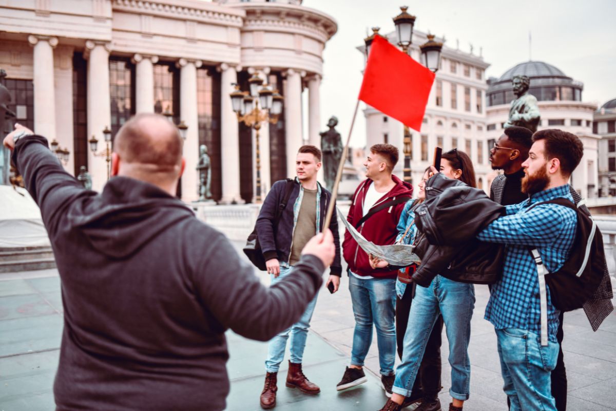 The image shows a group of people and a man holding a flag which means a tour guide is great for outgoing people who enjoy sharing stories and meeting new people.