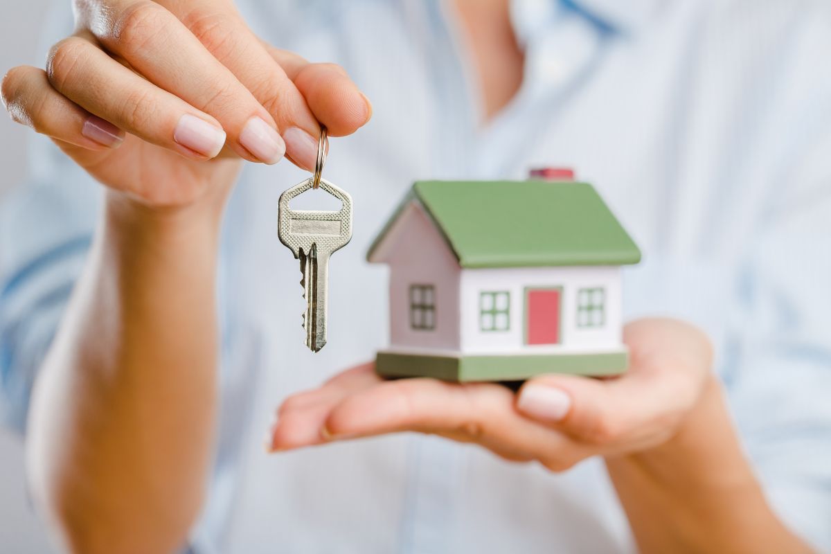 The photo shows a girl's hand holding a key and a mini house which means that becoming a house sitter is a good way to make extra money without having to do much work.