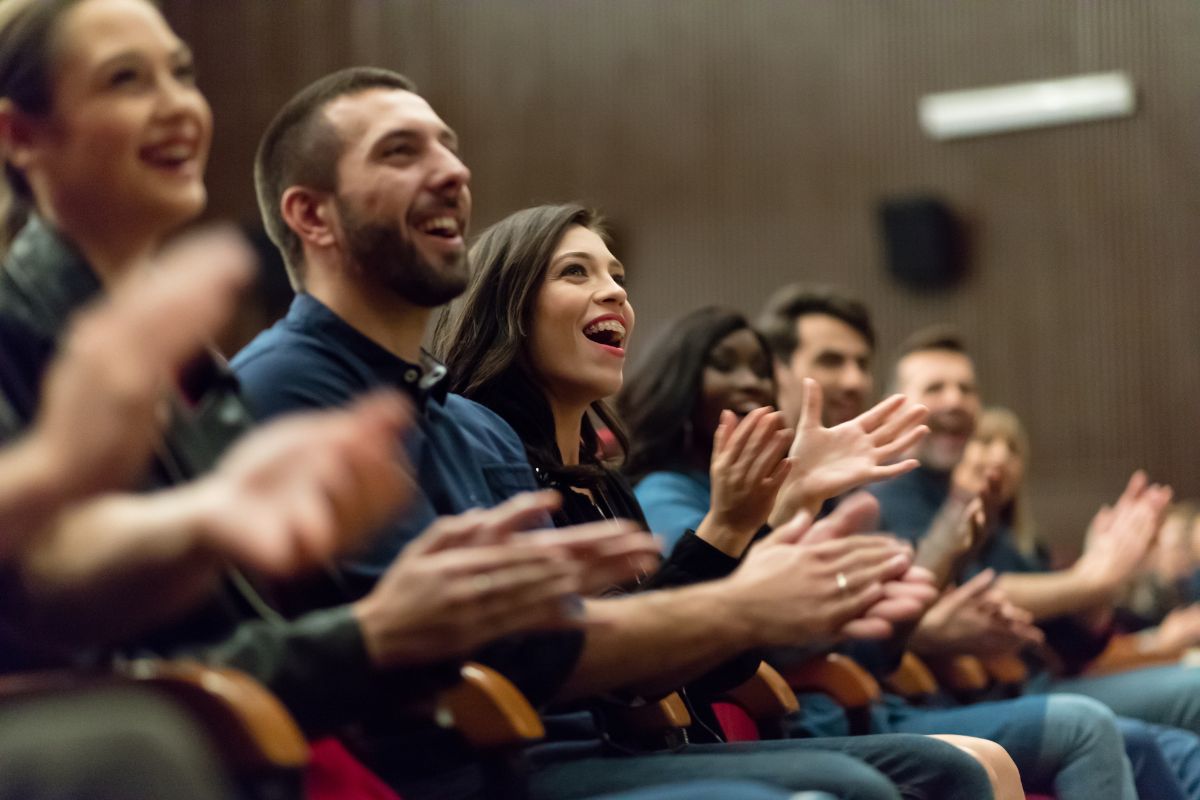 The image shows a group of people clapping together referring to an event extra as an easy way to earn money without a long-term commitment.