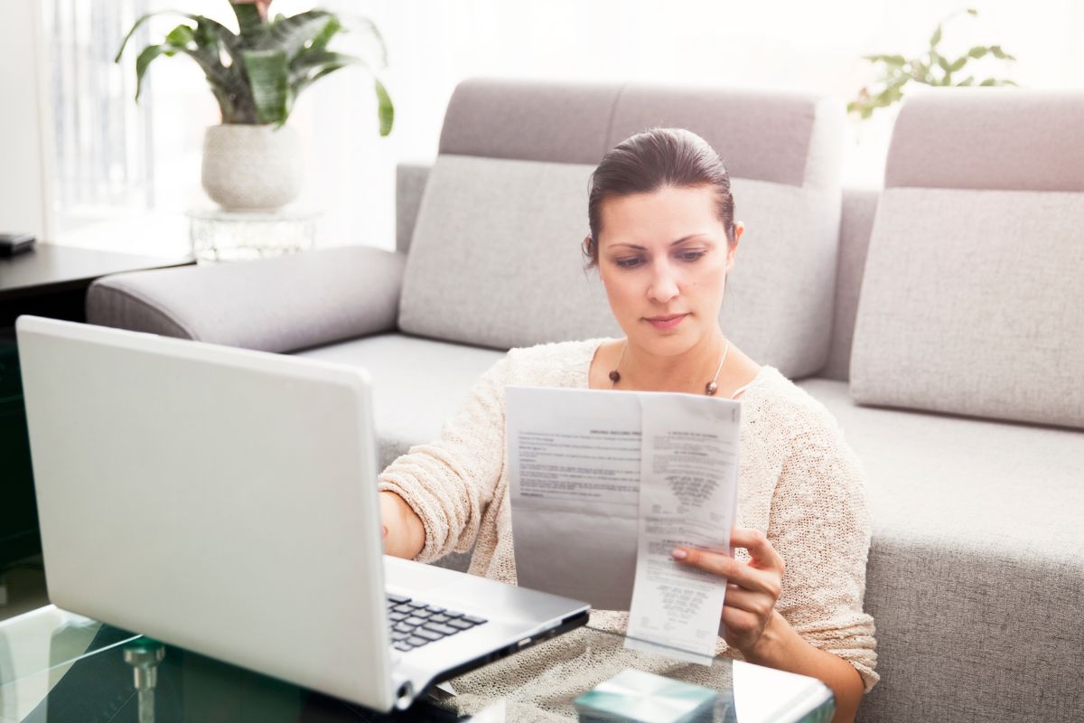 The image shows a girl using a laptop while looking at the paper which means filing under the wrong status can mean a higher bill that could have been avoided.