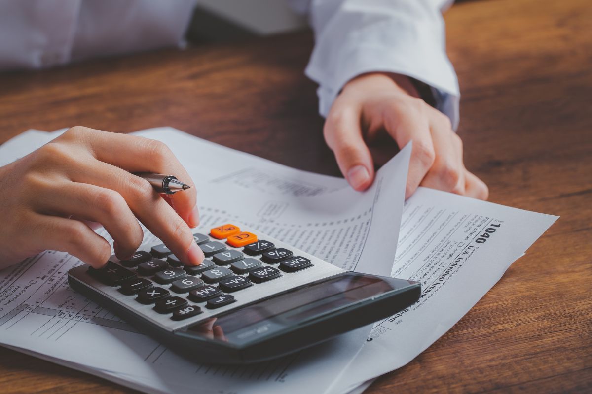 The image shows a girl's hand holding papers while calculating which means not contributing to pre-tax accounts might be paying more to the IRS than you have to.