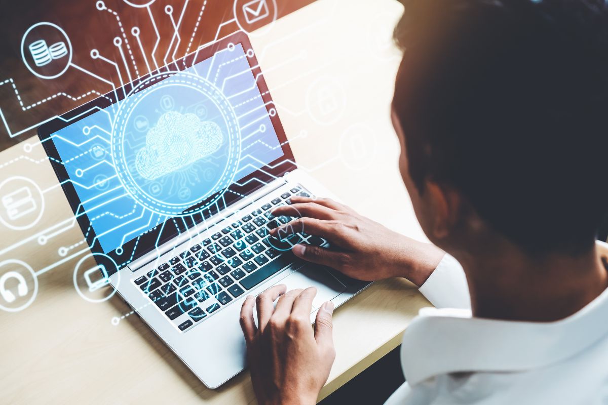 The picture tells about a man using a laptop with a screen display and visual icons indicating that a cloud computing job allows managing cloud infrastructure for companies is one of the in-demand skills with a passive income.