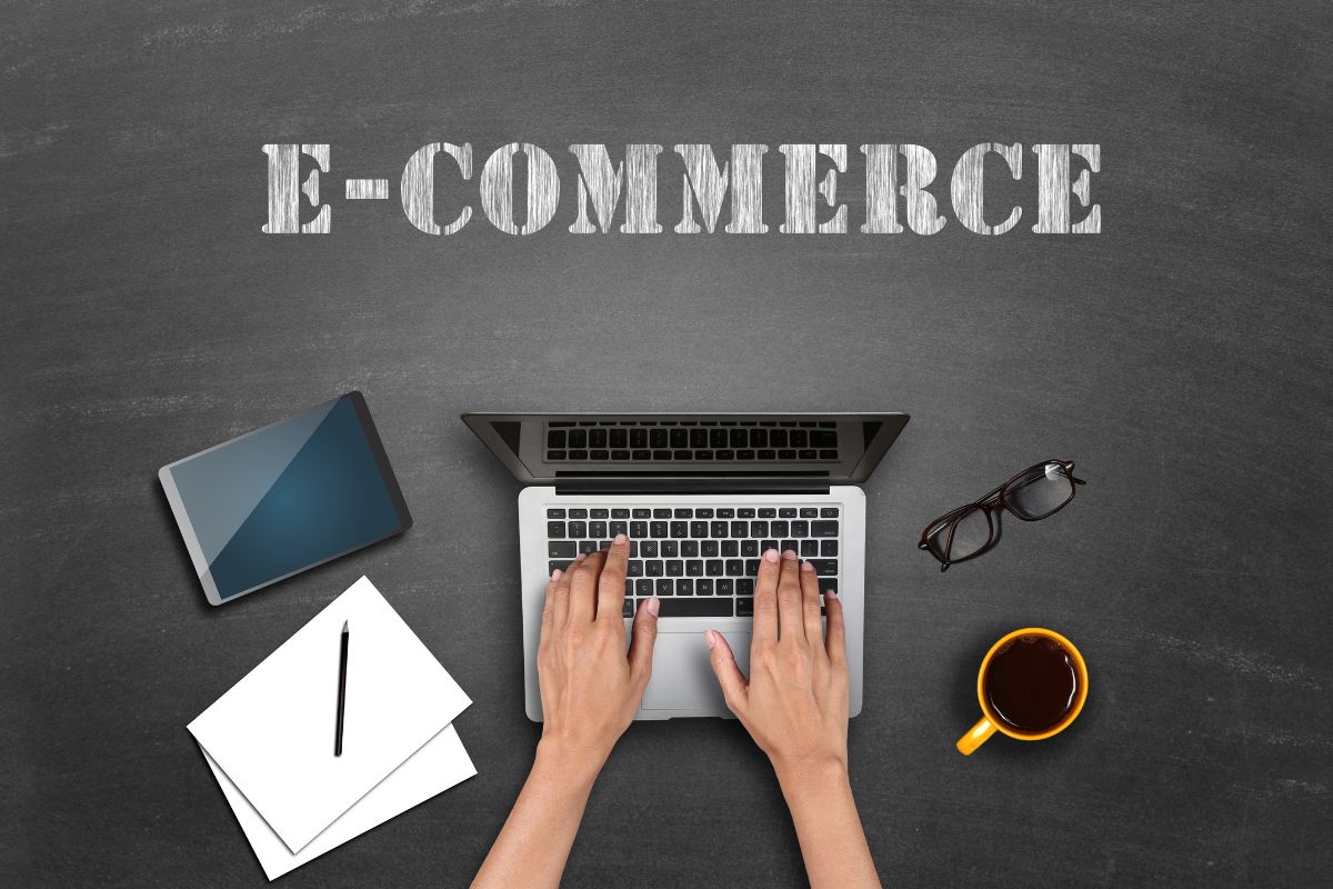 The picture shows a tablet device, an eyeglass, coffee, papers with a pen, a girl's hand using a laptop, and notes on the wall which means E-commerce and drop shipping selling products online is one of the in-demand skills help make money while staying at home on flexible time.