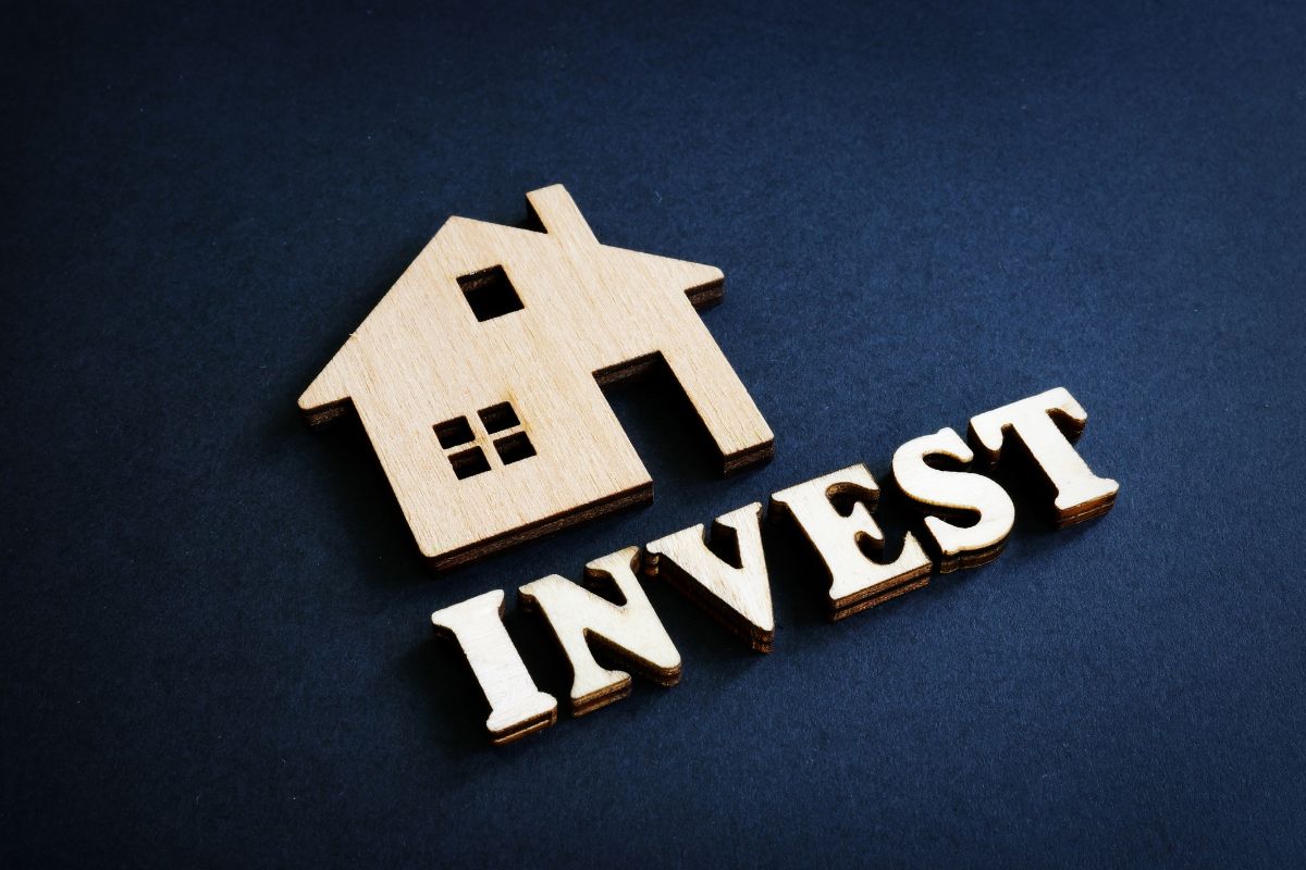 The photo tells about a wooden mini house and a note which means real estate investing and property helps to grow money by flipping homes, rental properties, and more.