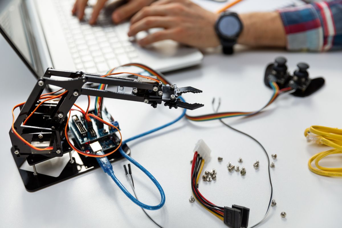 The image shows screws, cables, metal parts, and a man typing on the keyboard referring to automation and robotics allowing to develop of robotic solutions for industries and in-demand skills with earning potential.