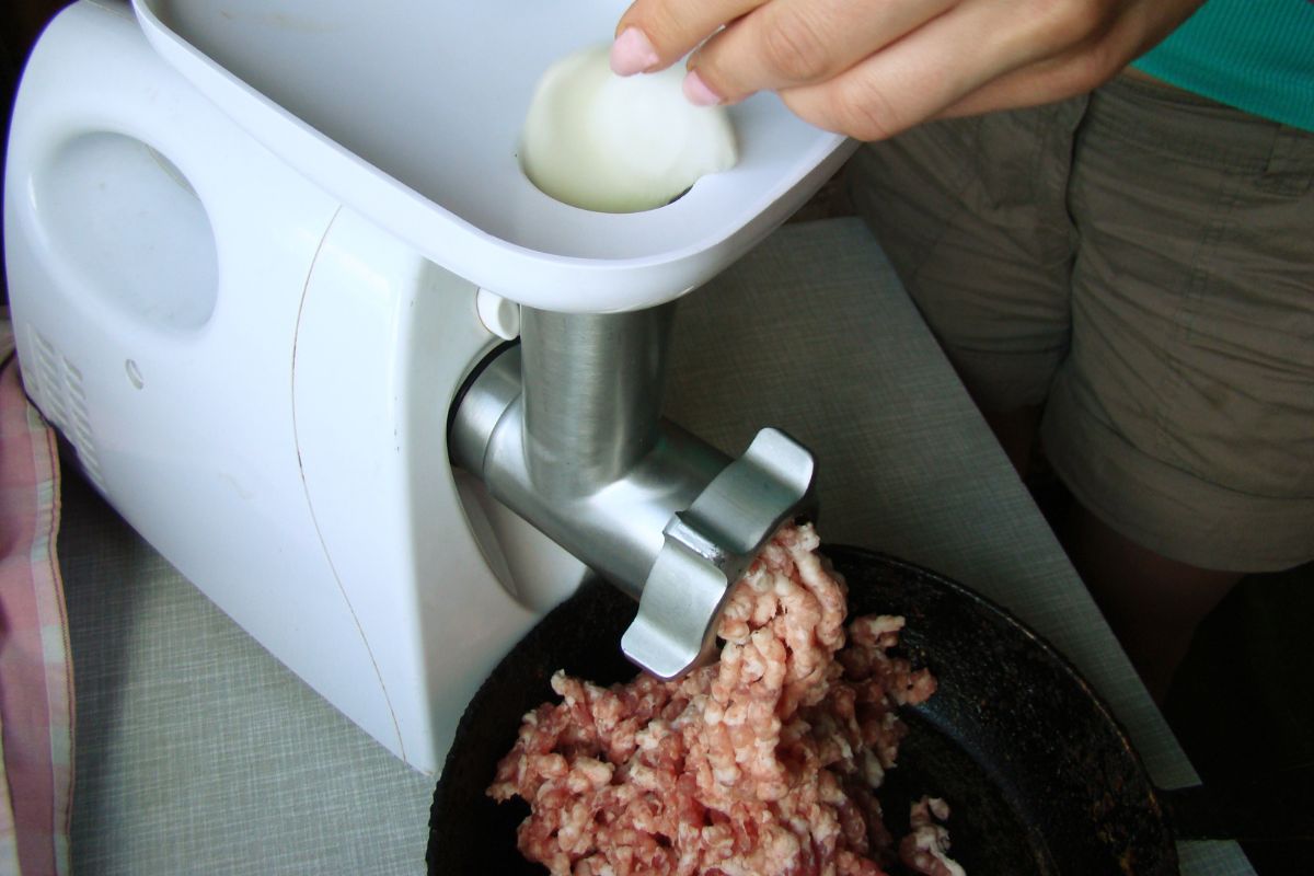 The image shows a girl's hand putting meat into an machine which means that grinding your meat at home is cheaper than pre-ground options that save money on groceries.