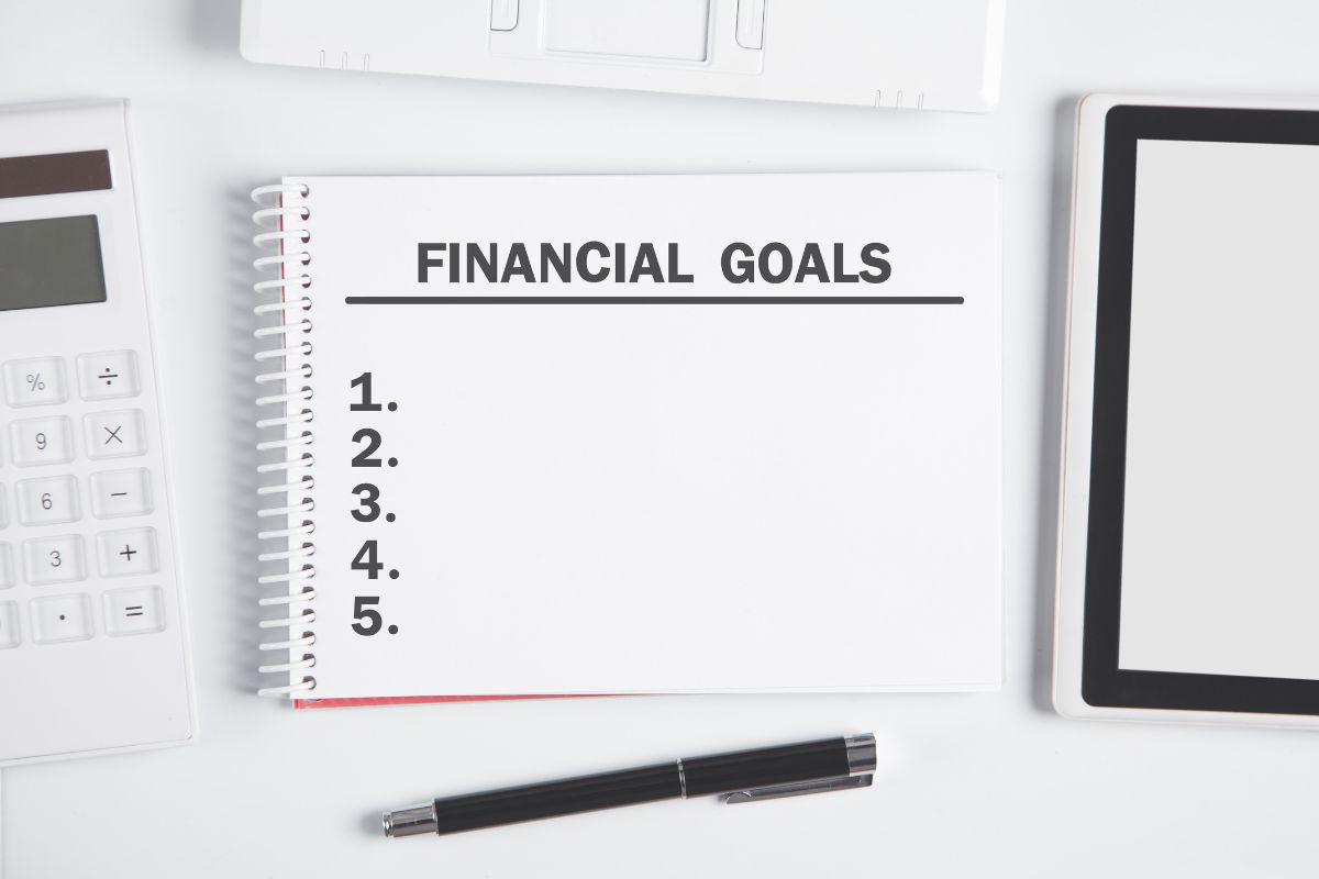 The picture shows a calculator, a pen, and a notebook with notes which means reviewing financial goals every morning helps to stay on track and avoid wasting money on things that don't matter.