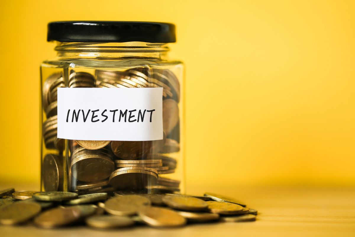 The photo tells about coins on the table and a jar filled with coins and with a note indicating to invest daily even small amounts grow into wealth over time.