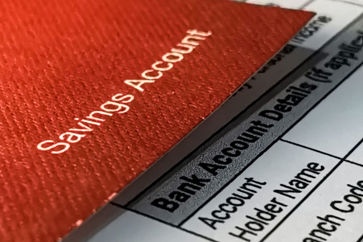 The photo shows a bankbook with a piece of paper with notes indicating that using the out-of-sight, out-of-mind method is great for building solid emergency fund savings without overthinking it.
