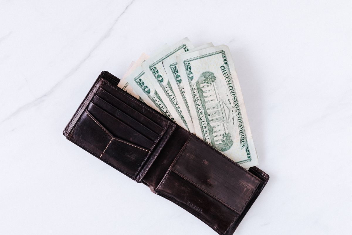 The photo shows a wallet with dollar bills indicating that challenging yourself to a buy nothing week can show how much money slips through the cracks.