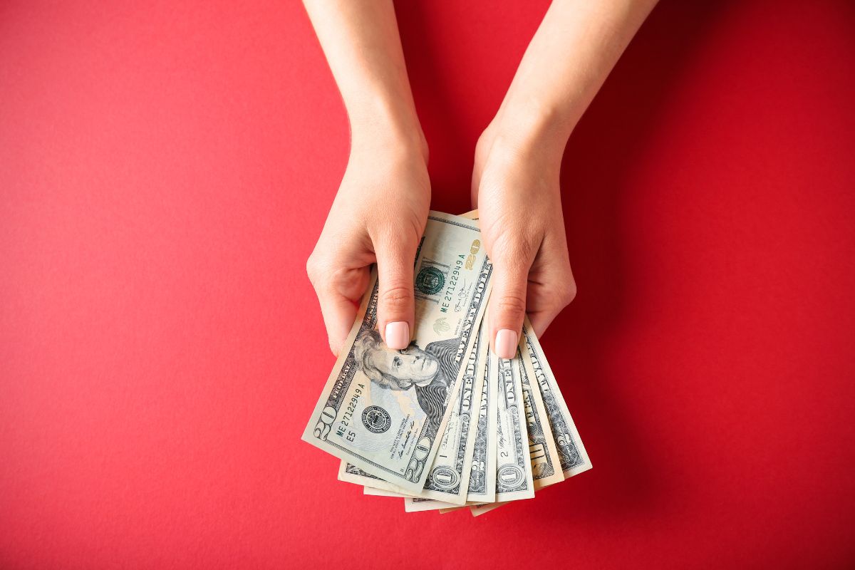 The image shows a girl's hand holding dollar bills which means assigning every dollar to a job helps keep savings on track while still allowing room for things you enjoy.