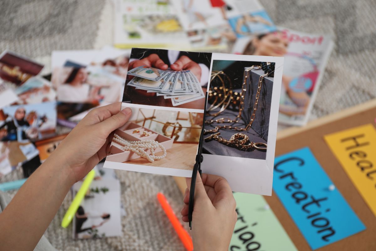 The photo tells about magazines, photos, a board with notes, and a girl's hand cutting the pictures indicating to make a vision board of what saving money keeps goals in front of you and helps you say no to impulse buys that don't help you get there.