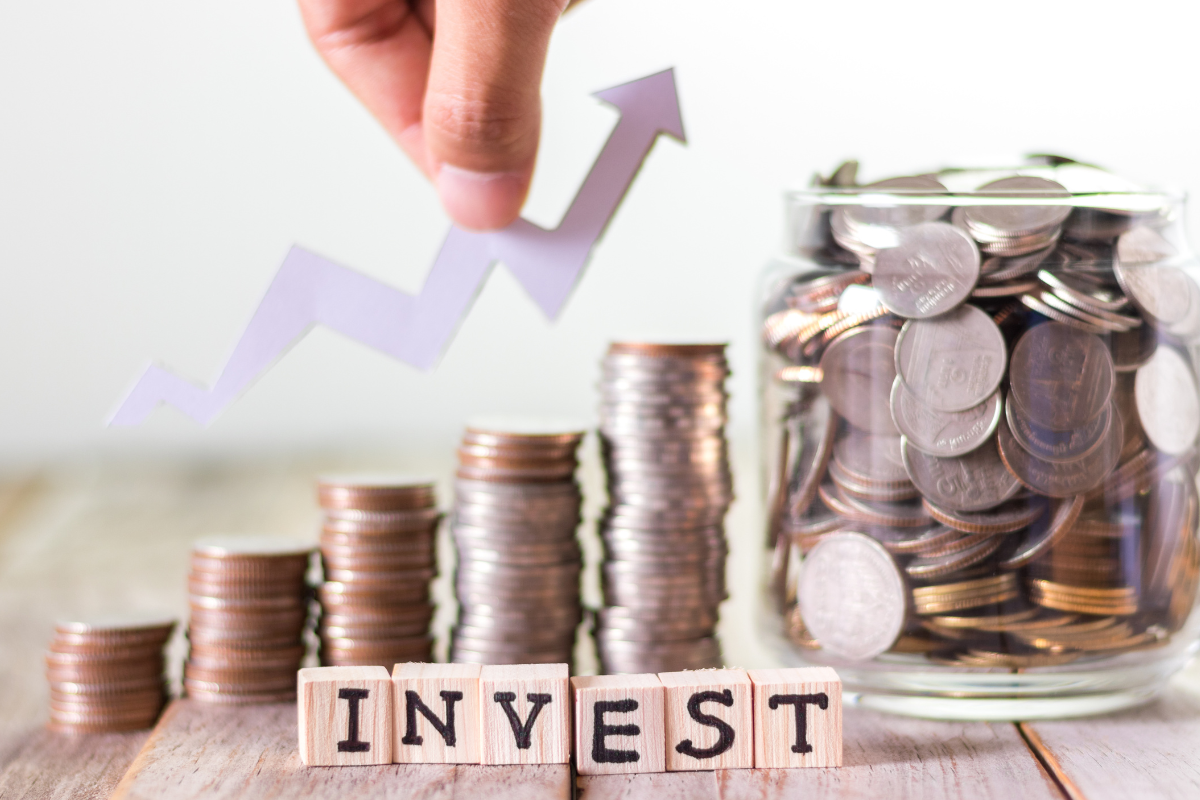Picture of jars with coins and invest wording on wooden cubes.