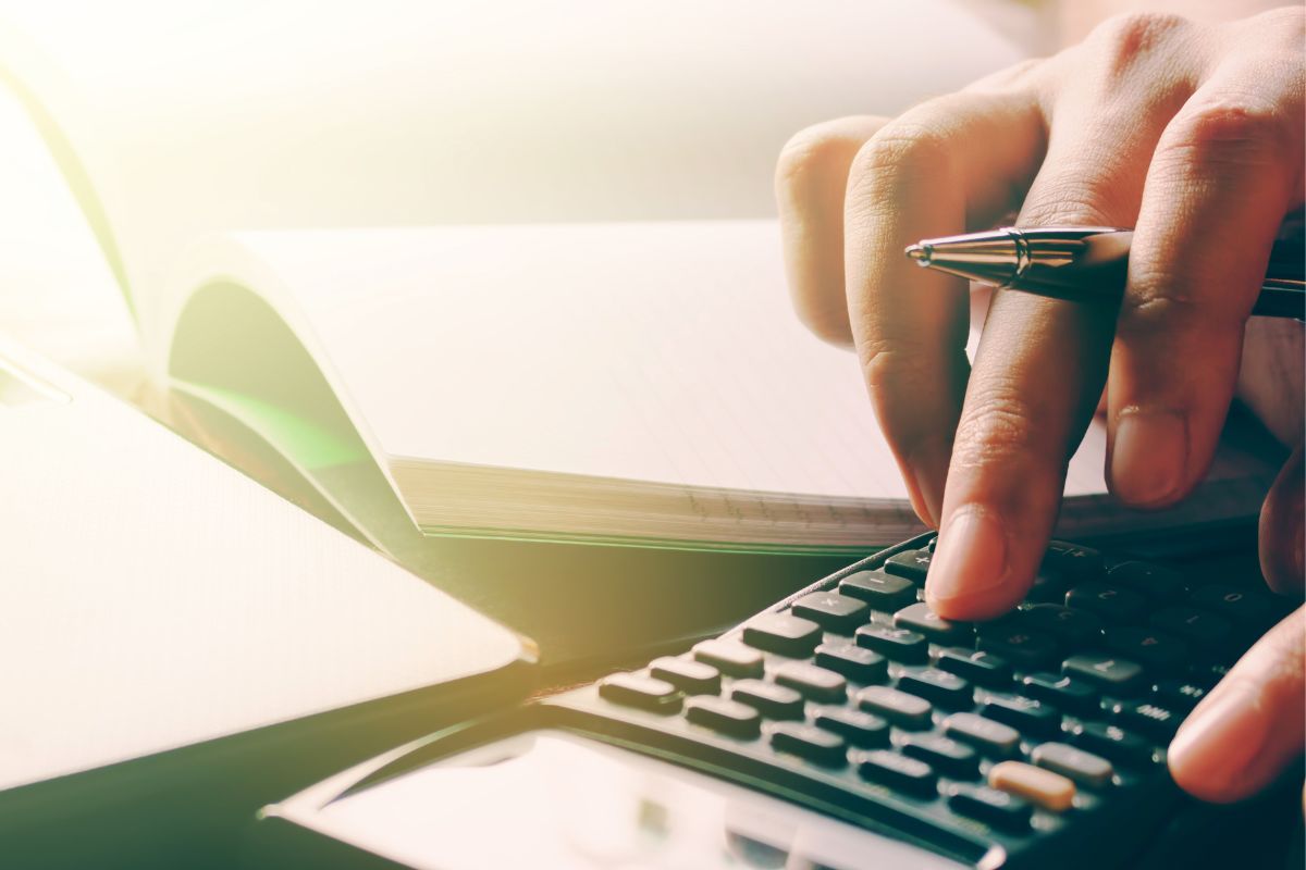 The photo shows a woman's hand calculating her budget.