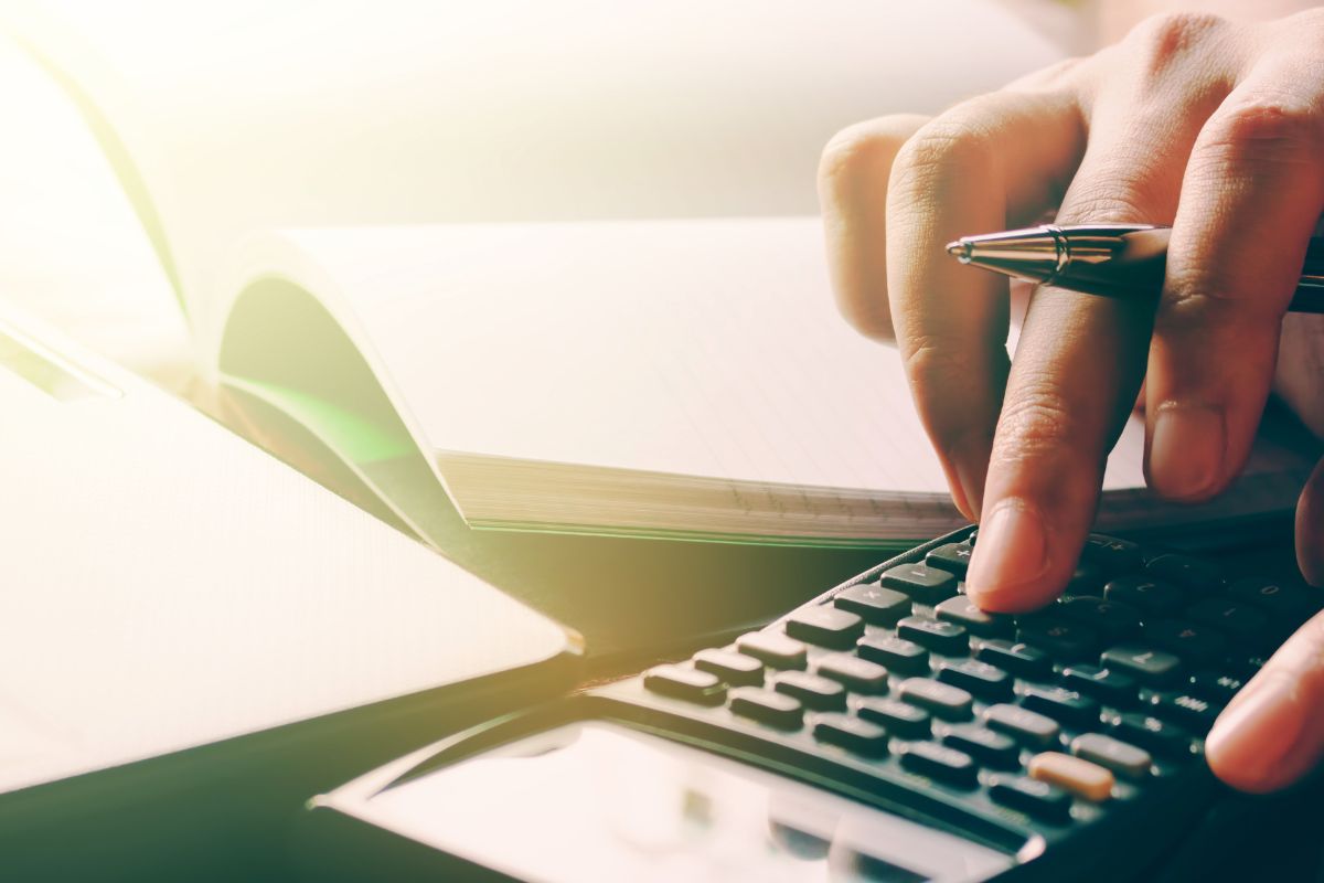 The picture tells about a notebook and a girl's hand calculating which means tricking yourself into saving by budgeting helps you build savings without effort.