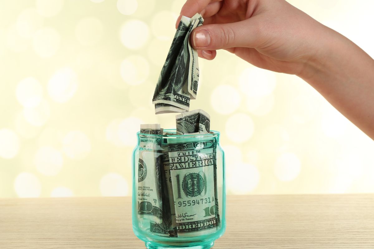 The picture tells about a jar filled with dollar bills and a girl's hand putting money inside which means that using a painful transfer system helps balance fun spending with financial growth.