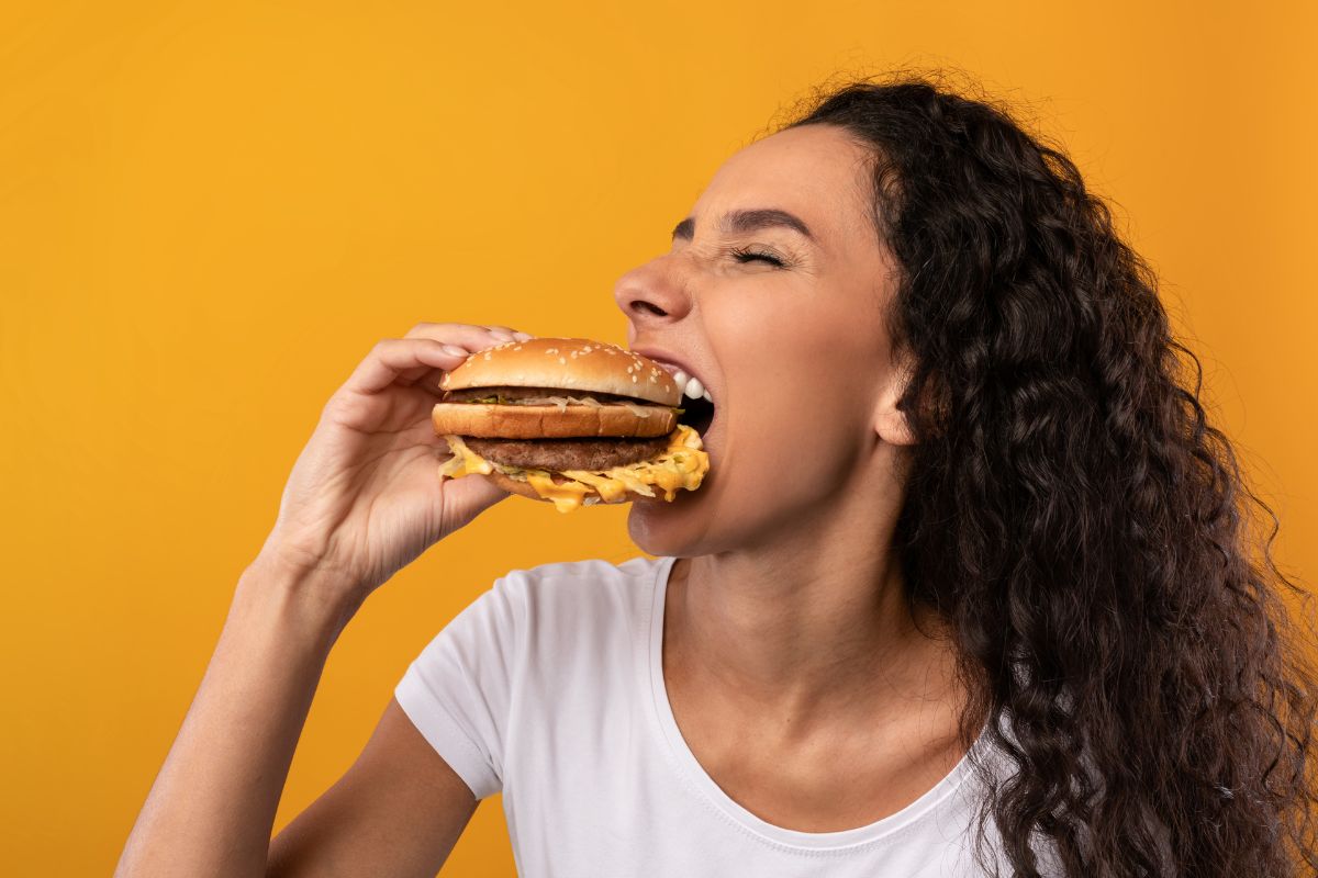 The image shows a girl eating a burger indicating to reward yourself for not spending keeps you motivated and makes savings feel like a win instead of a sacrifice.